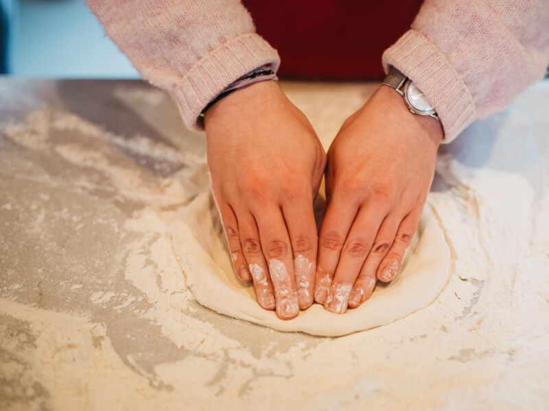 Hands pressing into pizza dough on a floured surface to make a circular pizza dough base 